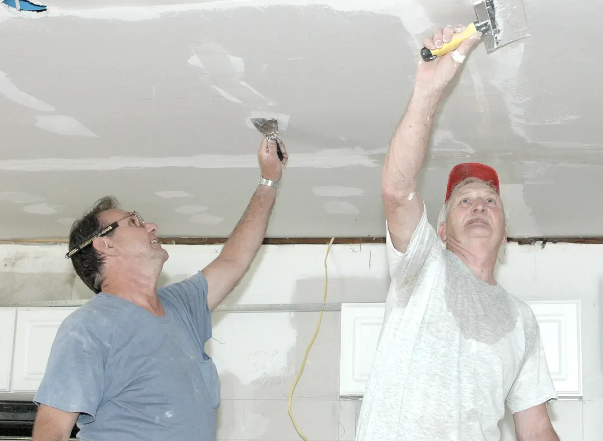 Voorbeeldfoto: twee mensen werken samen een plafond af met een spaan.