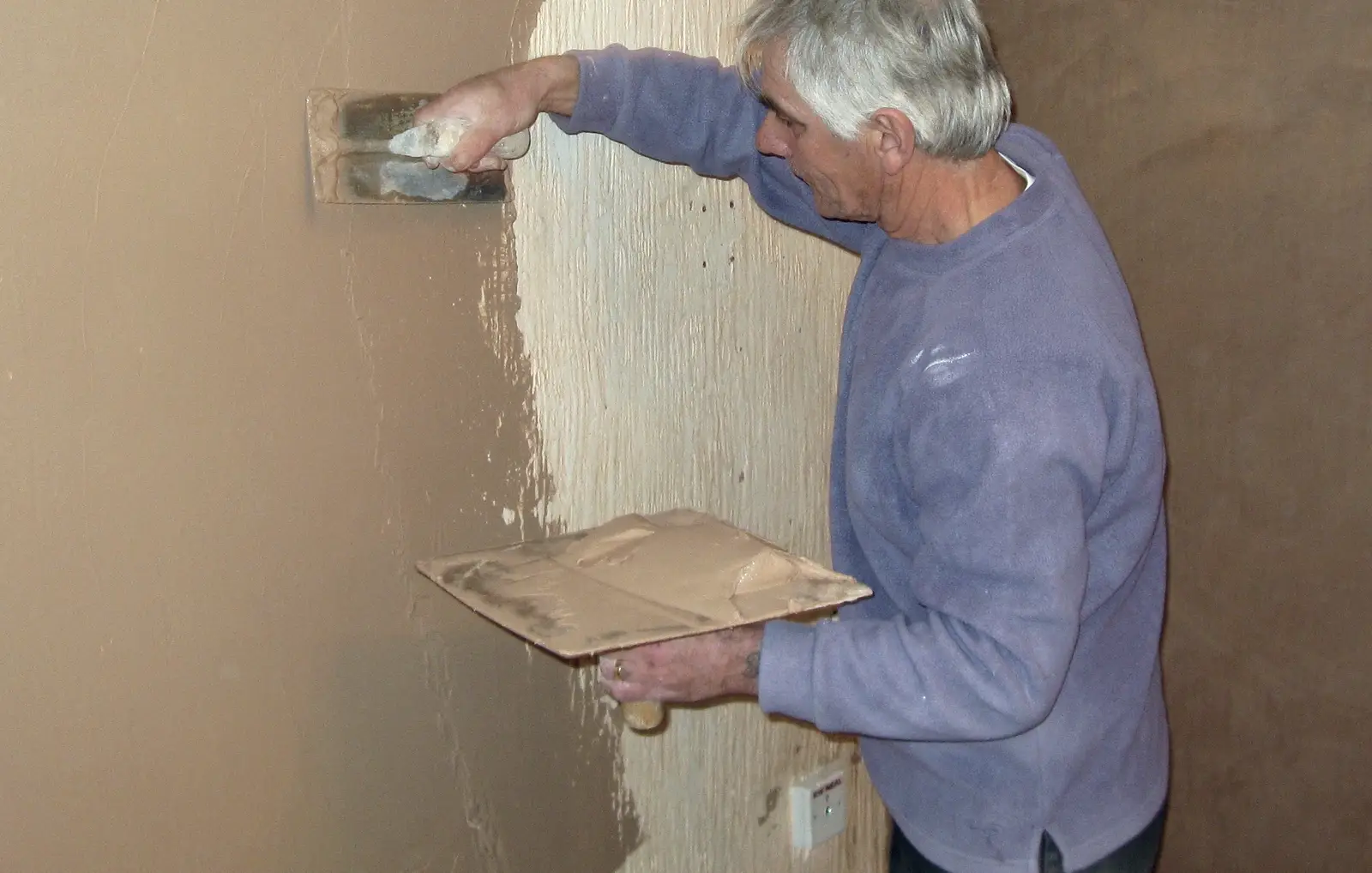 Voorbeeldfoto: een stukadoor werkt een wand bij met een spaan en een pleisterbord.